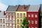 Maisons de ville multicolores alignées, chacune avec sa façade et son toit uniques. Un arbre se trouve au premier plan. Ciel dégagé.