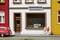 Un modèle miniature d'une rue avec un magasin nommé 'Bricoleur'. Deux petites figurines jouent devant la boutique. Une voiture rouge est stationnée à gauche.