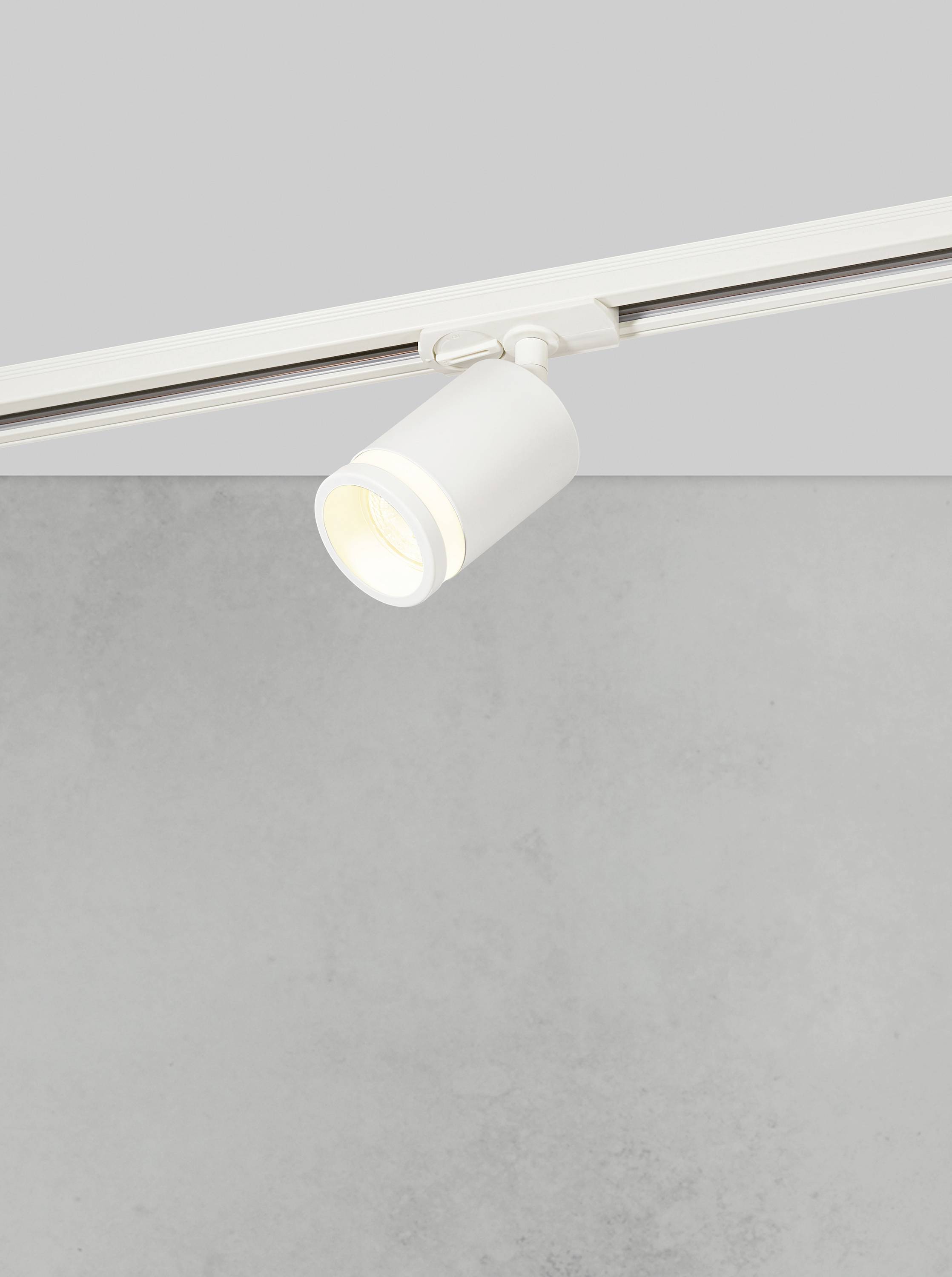 Projecteur de plafond blanc individuel monté sur rail, illuminant un fond gris.