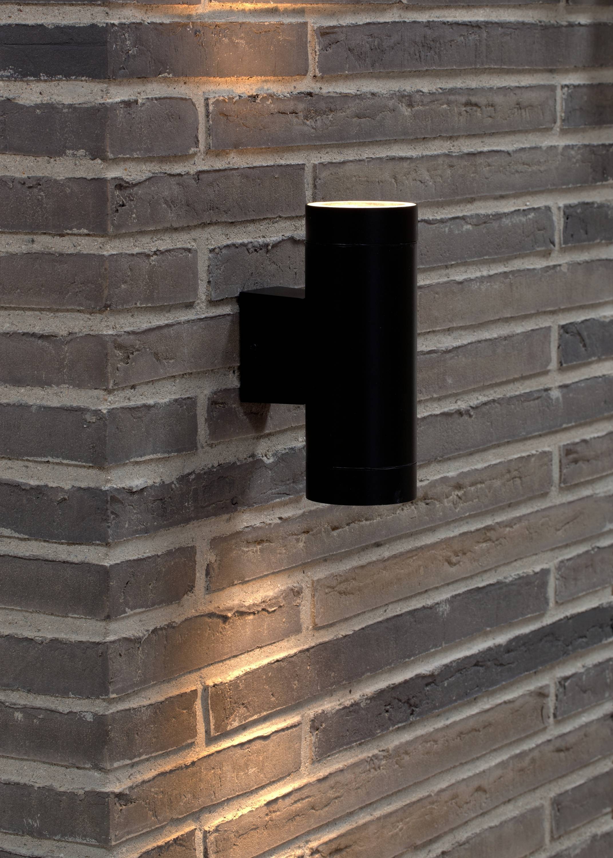 Une applique murale noire fixée à un mur de briques, éclairant vers le haut et vers le bas, crée une ambiance moderne.