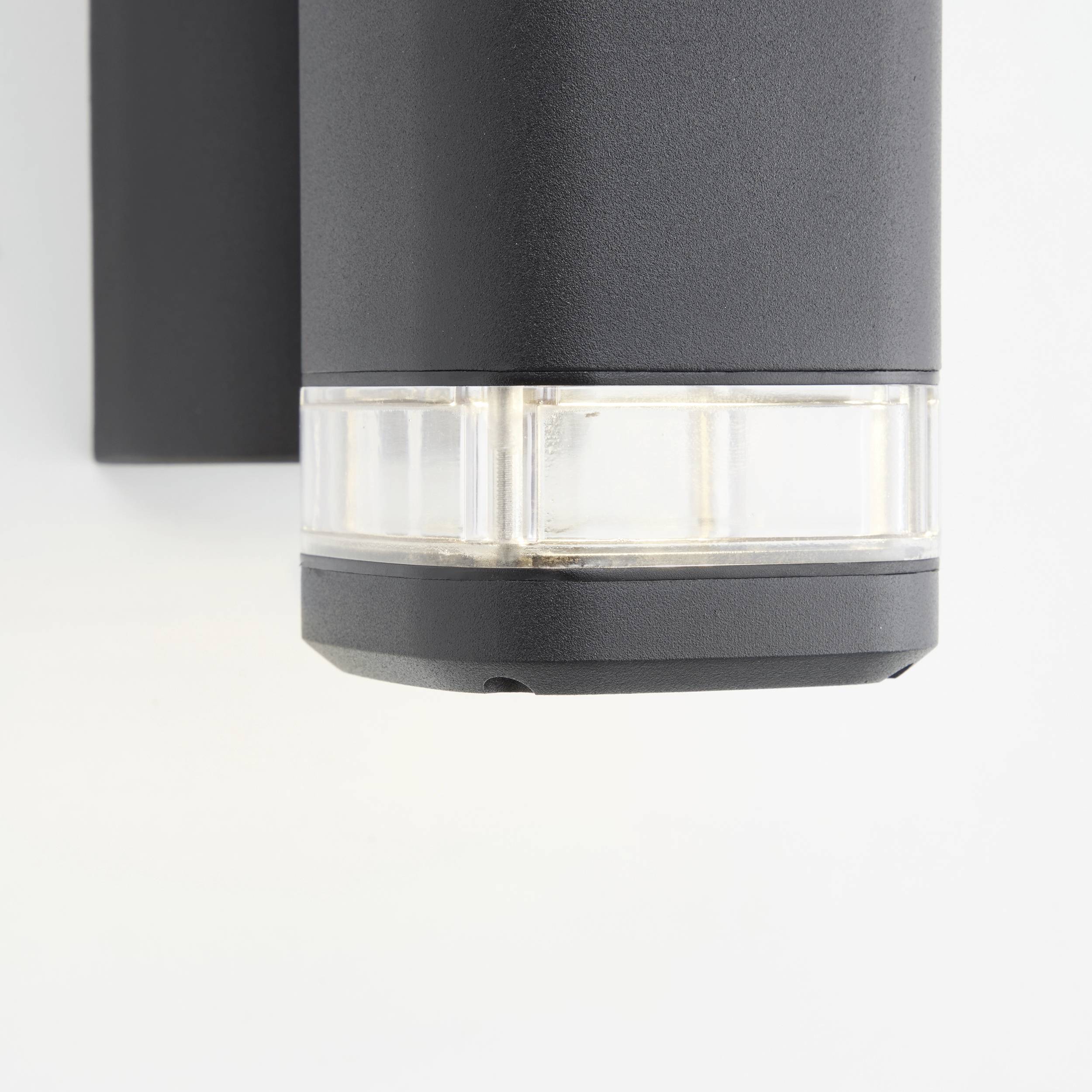 Lampe d'extérieur murale gris-noir avec ampoule transparente, fixée sur un mur blanc. Idéale pour les espaces extérieurs modernes.