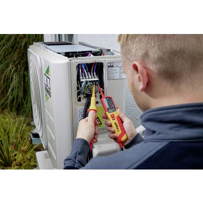 Un technicien vérifie les connexions électriques d'un climatiseur à l'aide d'un multimètre afin de s'assurer de la tension correcte.