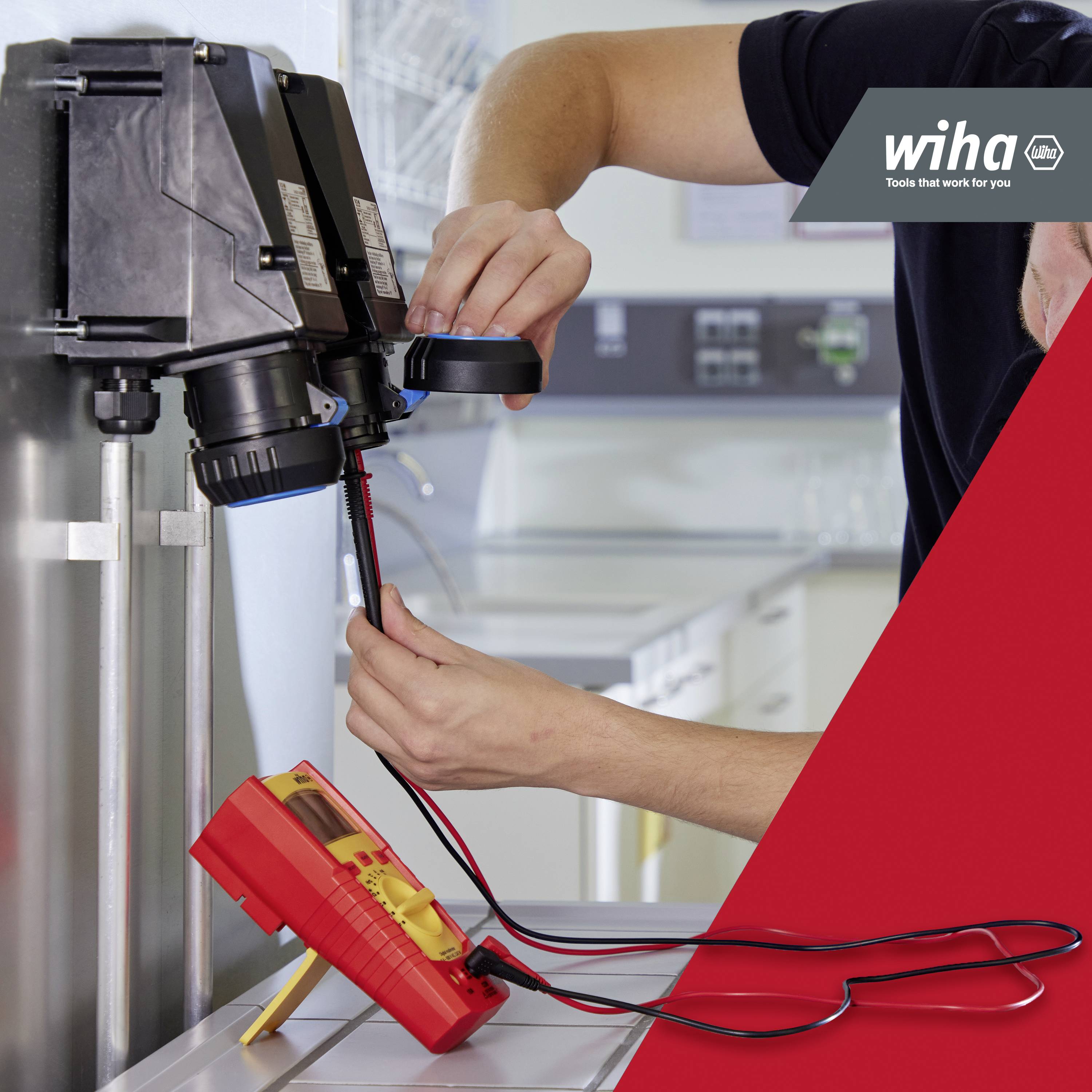 Un artisan utilise un testeur de tension sur une installation électrique dans un atelier. Le logo 'Wiha' est visible.