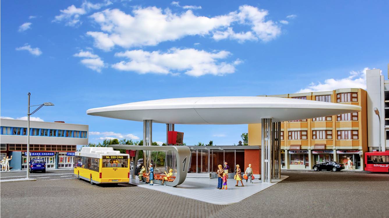 Des personnes se tiennent à un arrêt de bus futuriste avec un bus jaune au premier plan, des bâtiments modernes en arrière-plan, sous un ciel bleu.