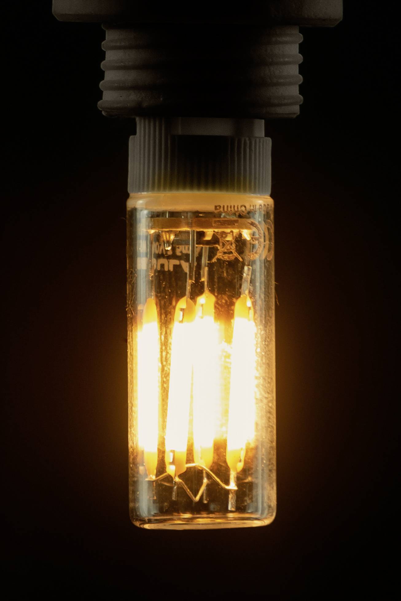 Une ampoule lumineuse avec des filaments visibles, émettant une lumière chaude et jaune, sur un fond sombre.