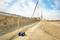 Un chantier avec une grue soulevant une grande dalle de béton. Un appareil de mesure est posé au sol au premier plan. En arrière-plan, on aperçoit une structure partiellement construite.