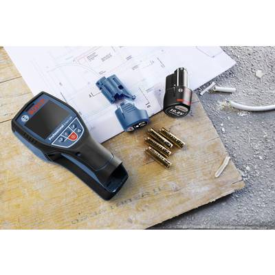 Un appareil de test numérique est posé sur un chantier à côté de plans, de batteries et de câbles. Il semble être utilisé pour des mesures techniques.