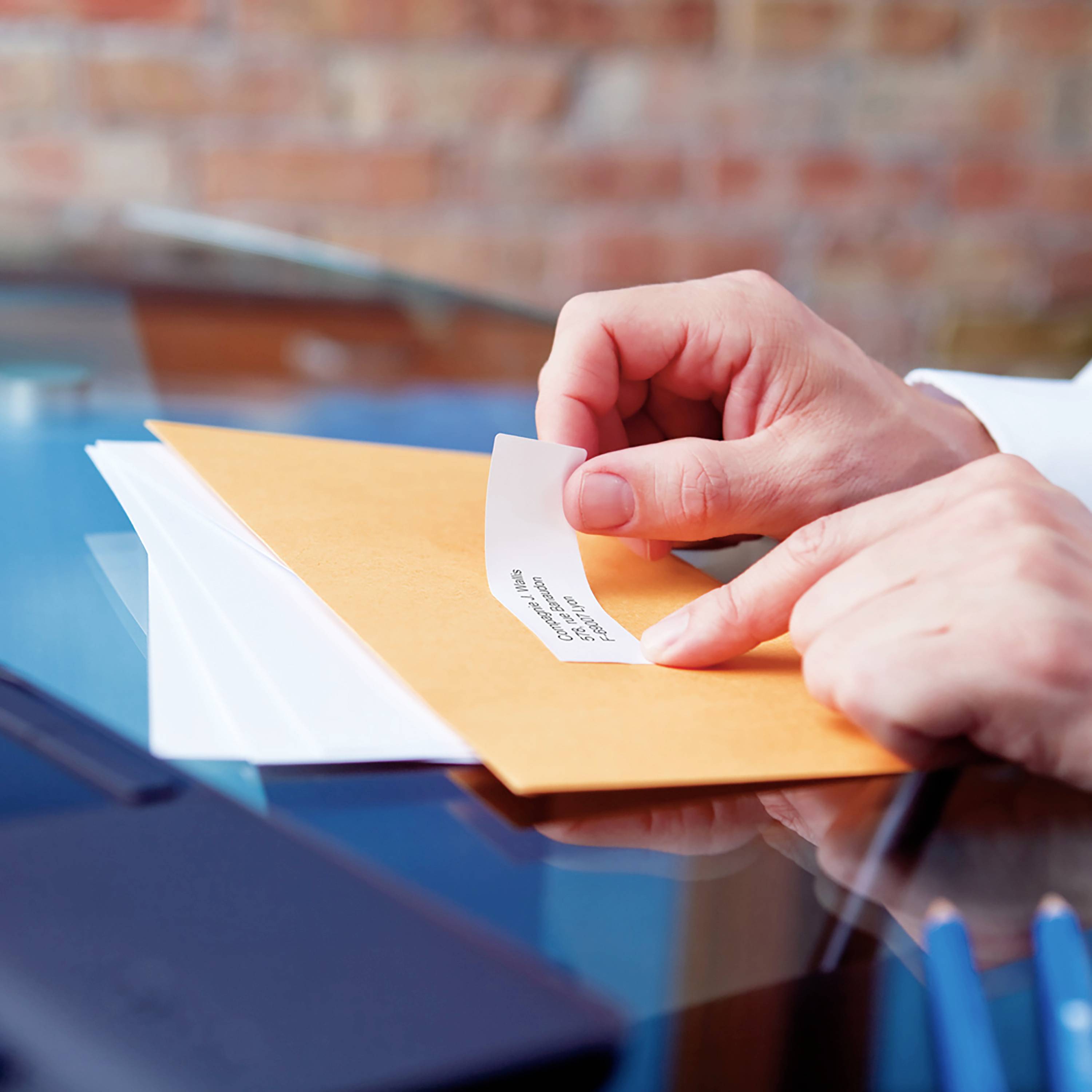 Une main ouvre une enveloppe orange avec une bande de papier insérée qui montre du texte. Elle se trouve sur une table.