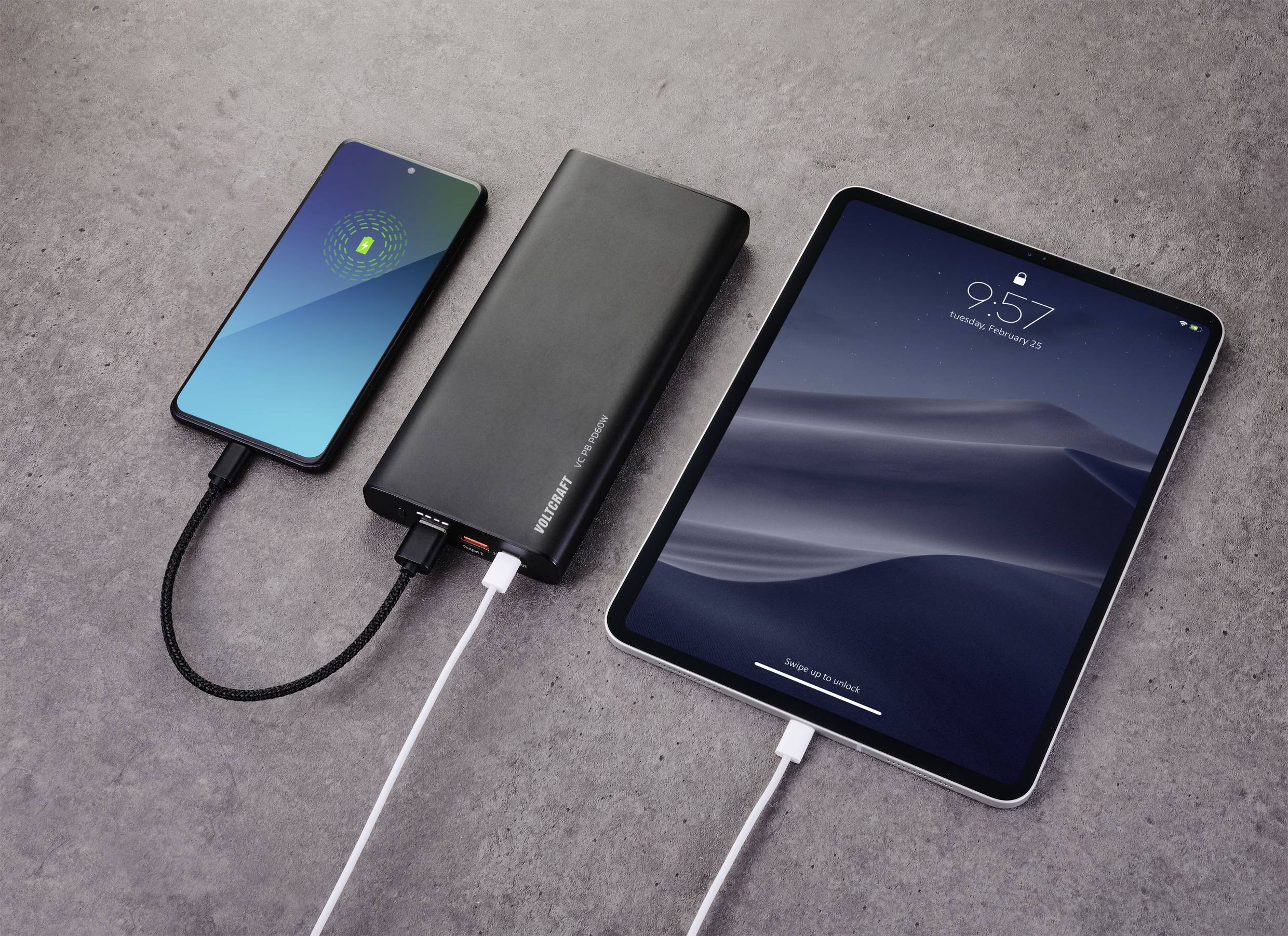 Un smartphone et une tablette sont connectés à une batterie externe par des câbles. Le smartphone affiche un scan d'empreinte digitale, la tablette indique l'heure 9:57.