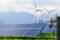 Panneaux solaires sur une prairie verte devant des montagnes avec des éoliennes en arrière-plan. Caméra de surveillance au premier plan. Thème : énergies renouvelables.