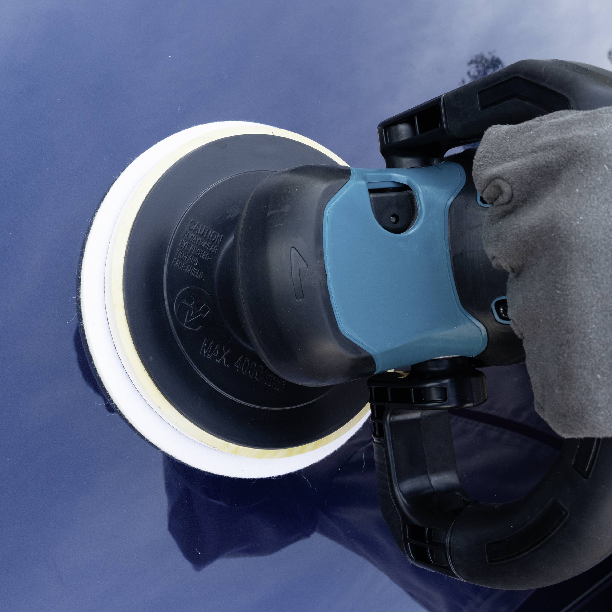 Une main tient une polisseuse sur une surface de carrosserie bleue afin de polir la peinture et de lui donner de l'éclat.