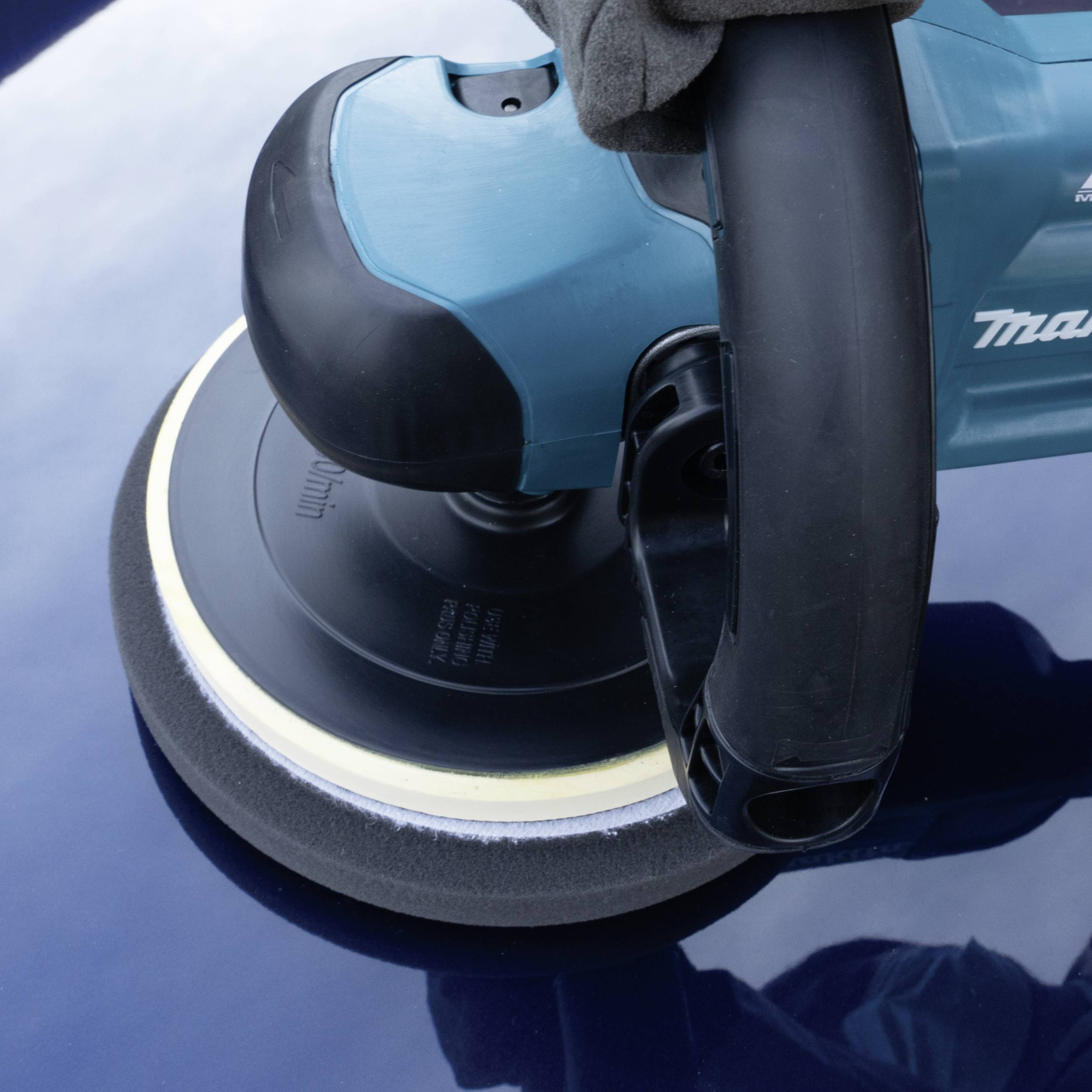 Gros plan d'un appareil de polissage bleu travaillant sur un revêtement de peinture automobile bleu foncé. Un chiffon doux est posé sur l'appareil.