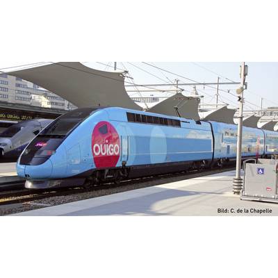 Un train à grande vitesse bleu portant l'inscription 'Ouigo' est stationné en gare. Un toit de gare et un autre train sont visibles sur la gauche.