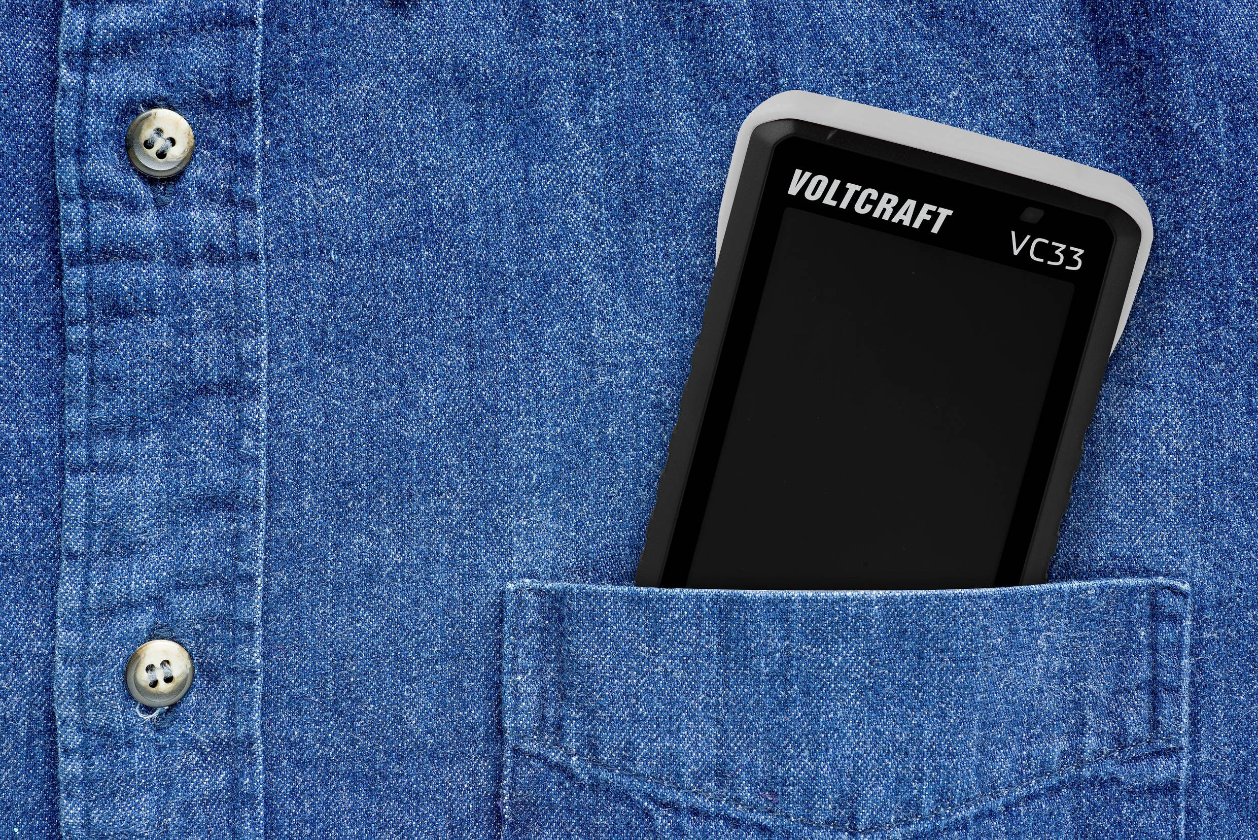 Un multimètre est glissé dans une poche de chemise bleue. Seule la moitié supérieure de l'appareil est visible. Le nom de marque 'Voltcraft VC33' est reconnaissable.