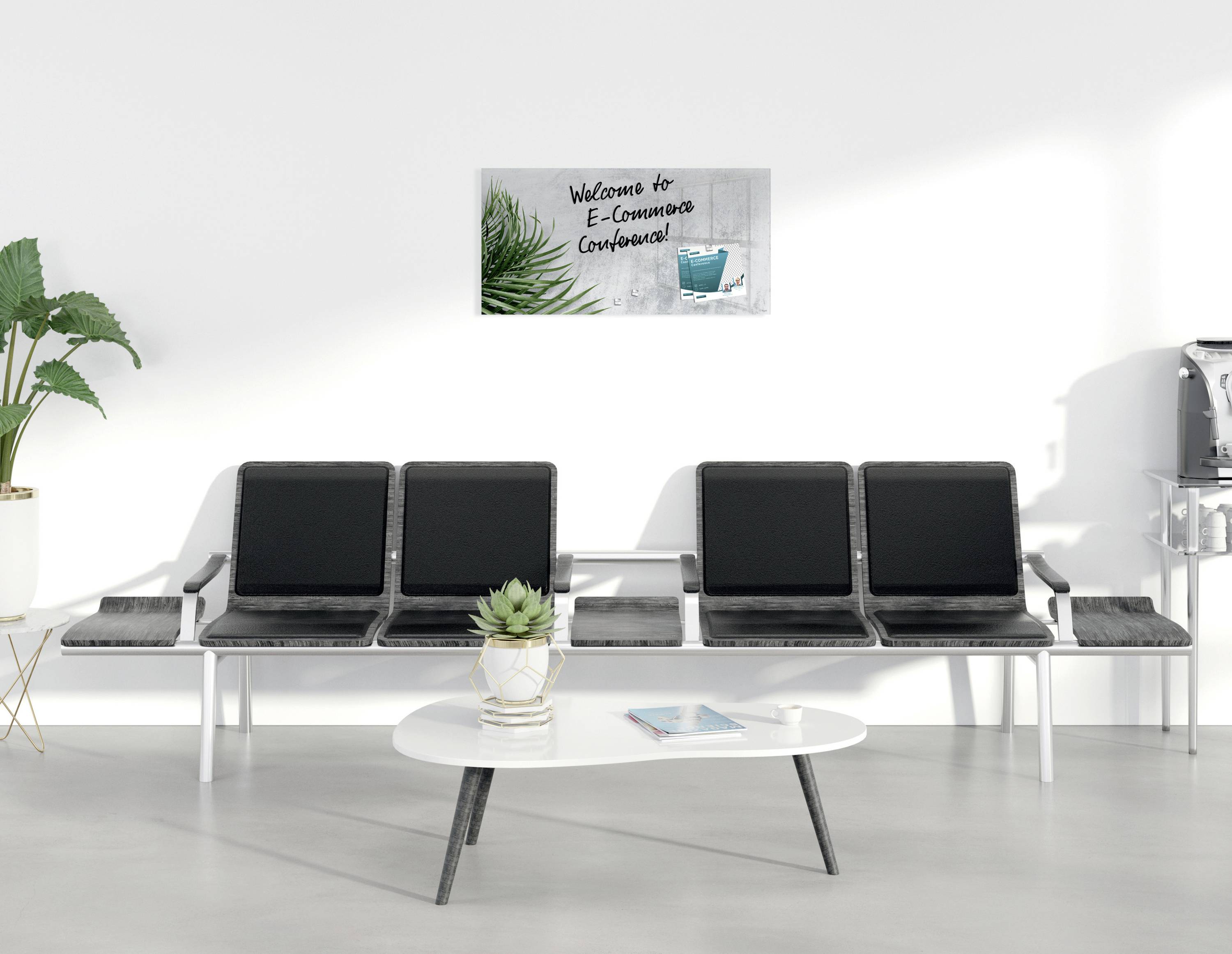 Salle d'attente avec quatre chaises grises, une table et des plantes. Sur le mur, un panneau indiquant « Bienvenue à la Conférence sur le Commerce Électronique ».