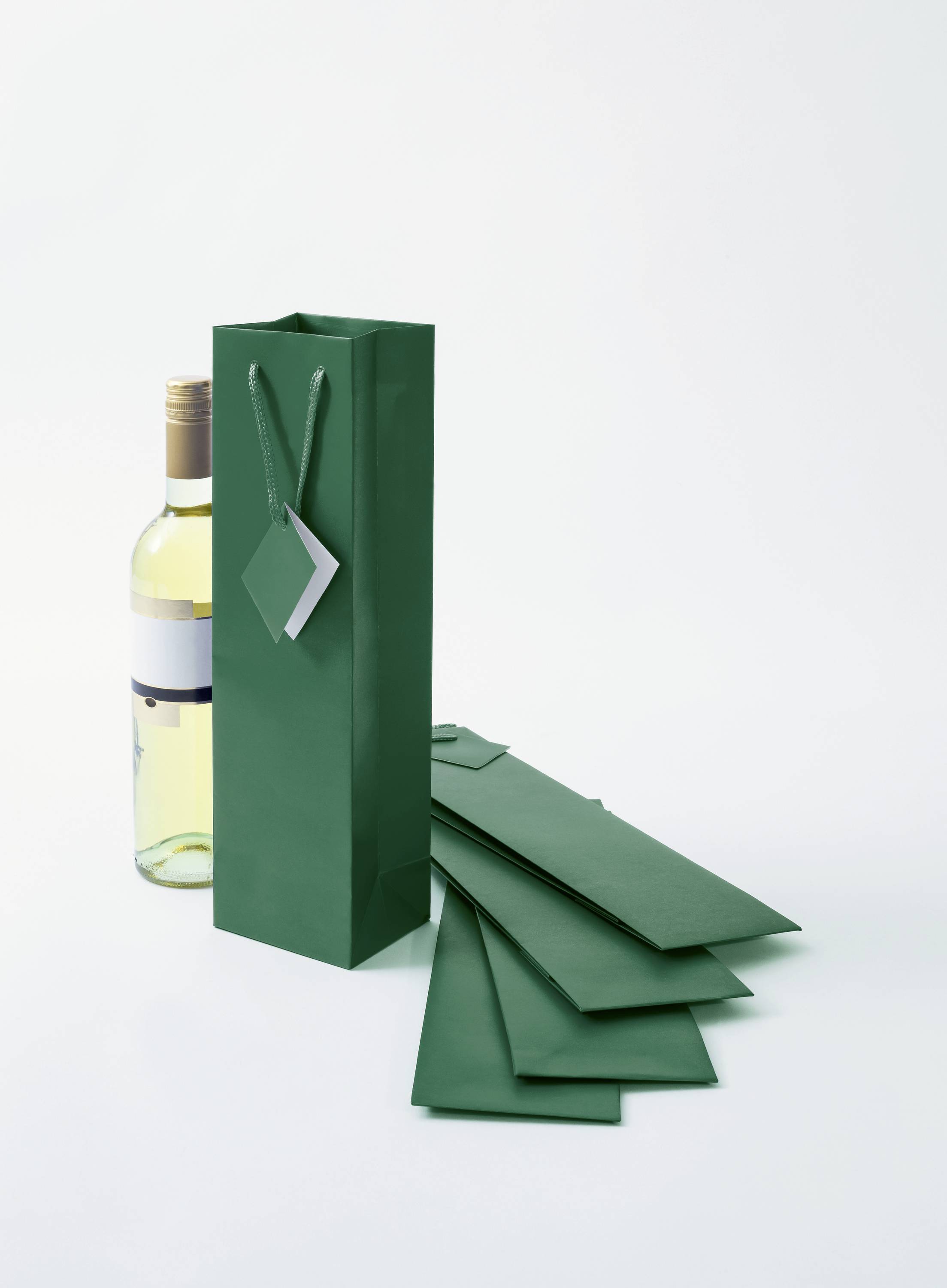 Sac cadeau vert à côté d'une bouteille de vin sur un fond clair.