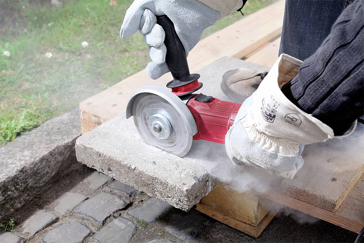 Une personne porte des gants de protection et utilise une meuleuse d'angle pour couper une dalle de béton sur une poutre en bois.