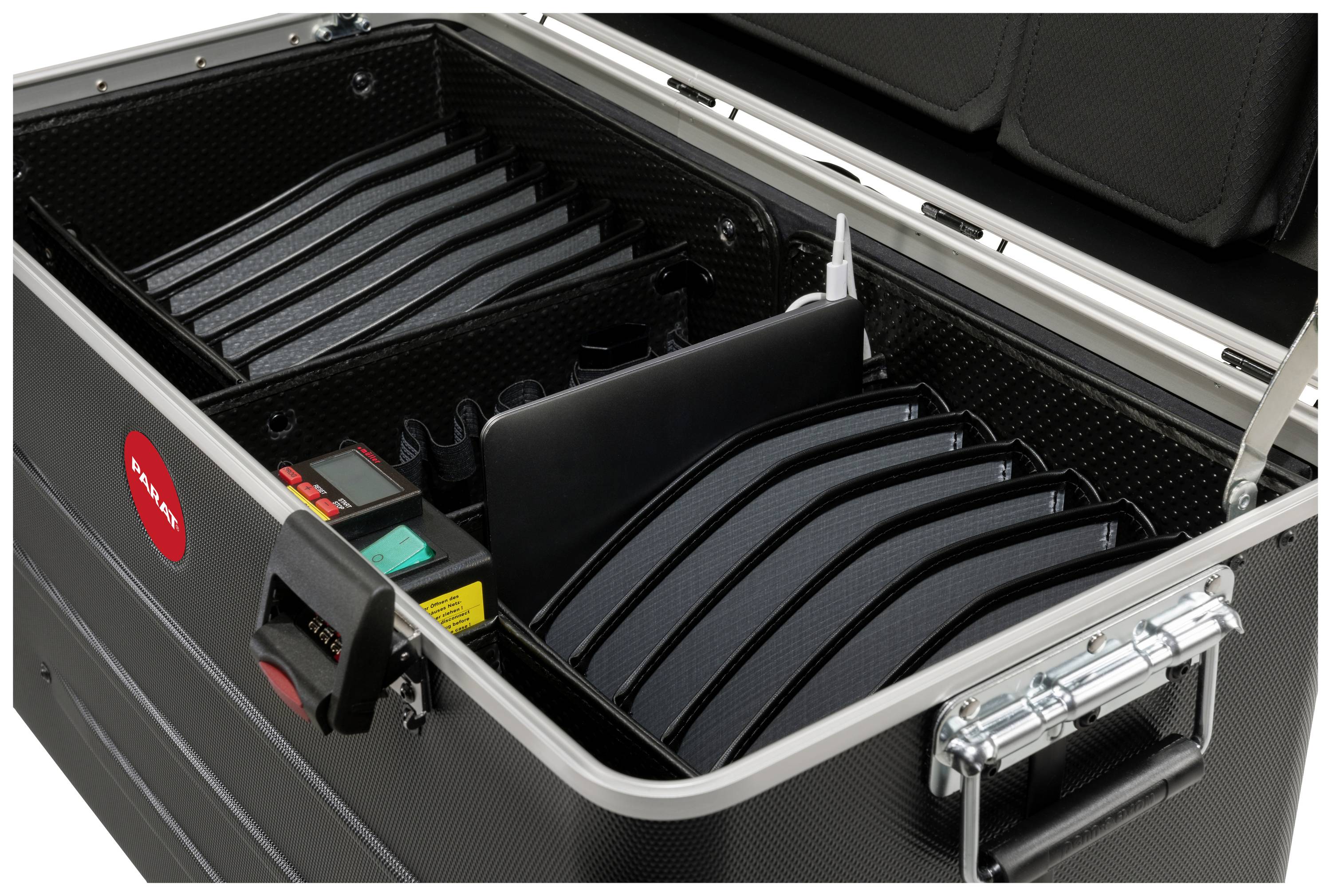 Valise noire ouverte avec plusieurs compartiments et une étiquette. Contient des accessoires techniques.