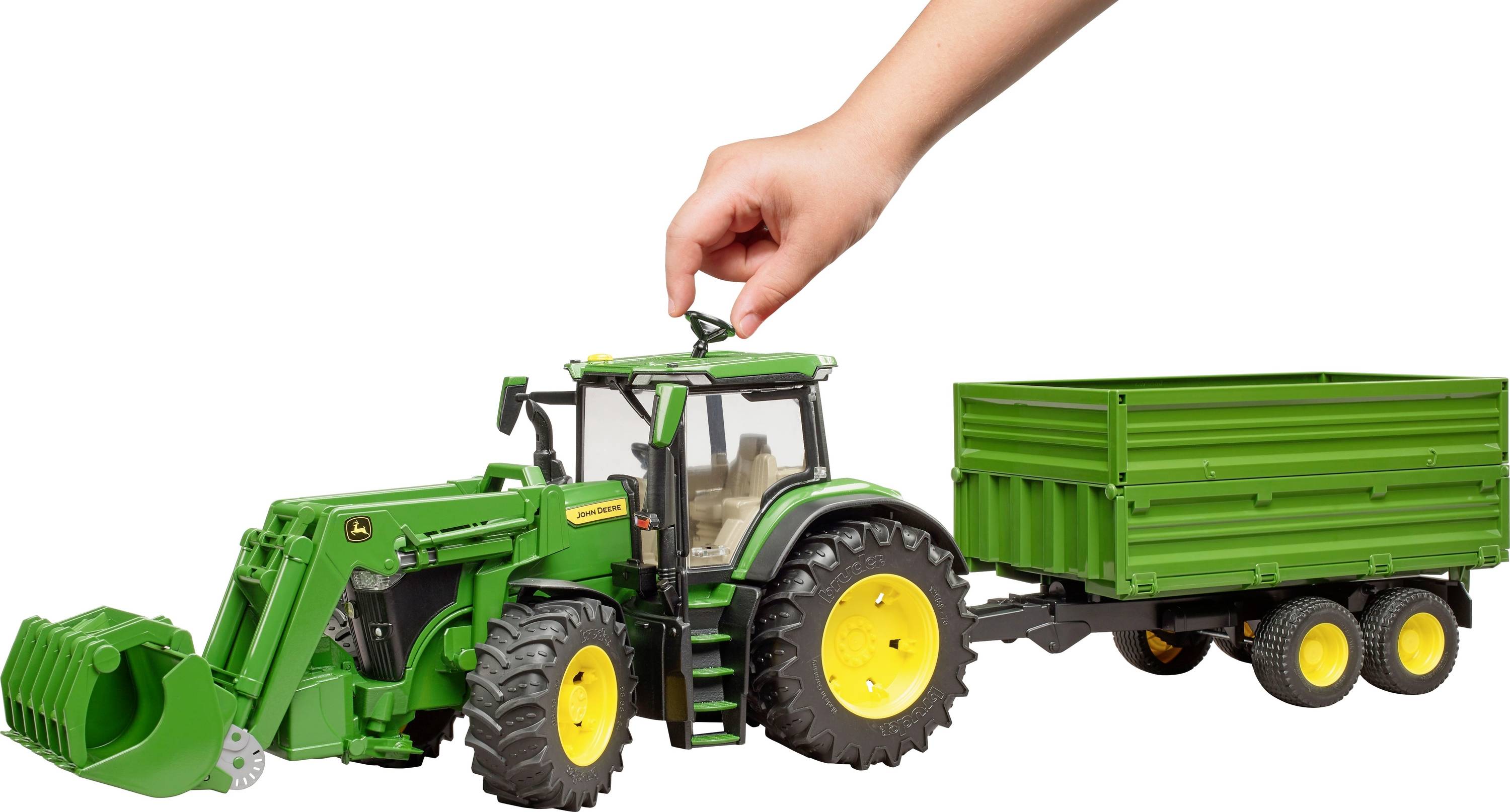 Une main soulève un tracteur-jouet avec sa remorque.