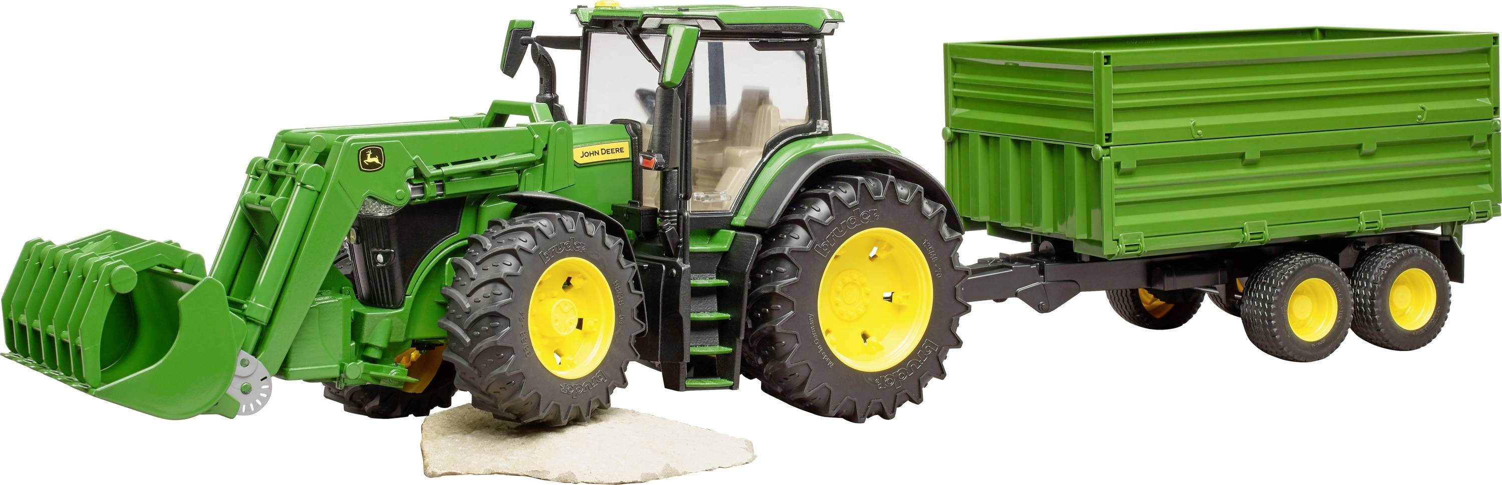 Tracteur jouet vert avec remorque, posé sur un fond blanc. Le tracteur soulève une plaque claire avec sa pelle avant.