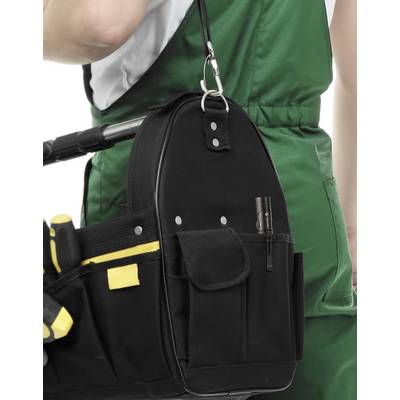 Un artisan en tenue de travail verte tient un sac à outils noir avec des outils jaunes et noirs à ses côtés.