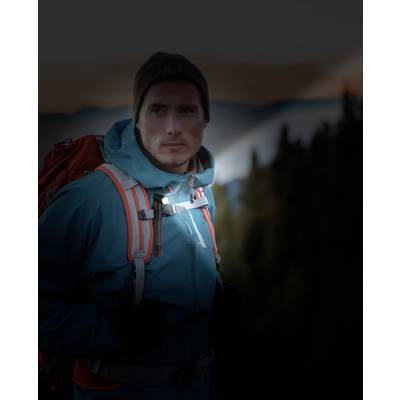 Un homme en tenue de randonnée et avec un sac à dos se tient dans un paysage montagneux au crépuscule. Il observe attentivement l'horizon.