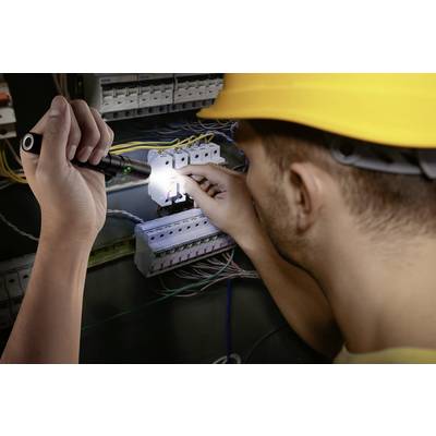 Un électricien portant un casque de sécurité travaille sur un armoire électrique ouverte. Il tient une lampe de poche qui éclaire le boîtier de fusibles.
