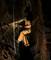 Une personne équipée pour l'escalade descend dans une grotte sombre à l'aide de cordes. Un casque avec lampe frontale éclaire le fond rocheux.