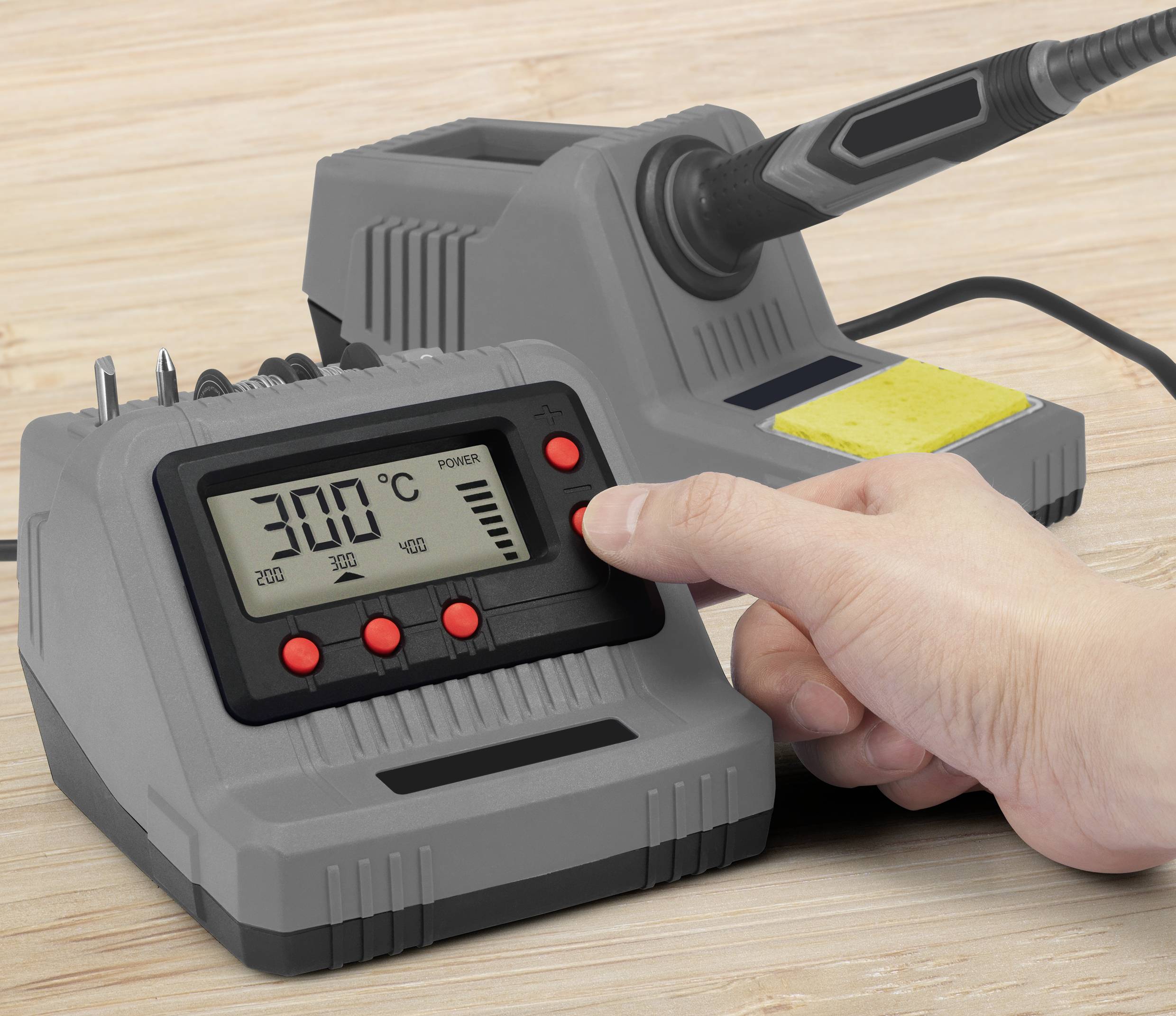 Une personne règle la température d'un poste à souder numérique à 300 degrés Celsius. Le poste se trouve sur une table en bois.