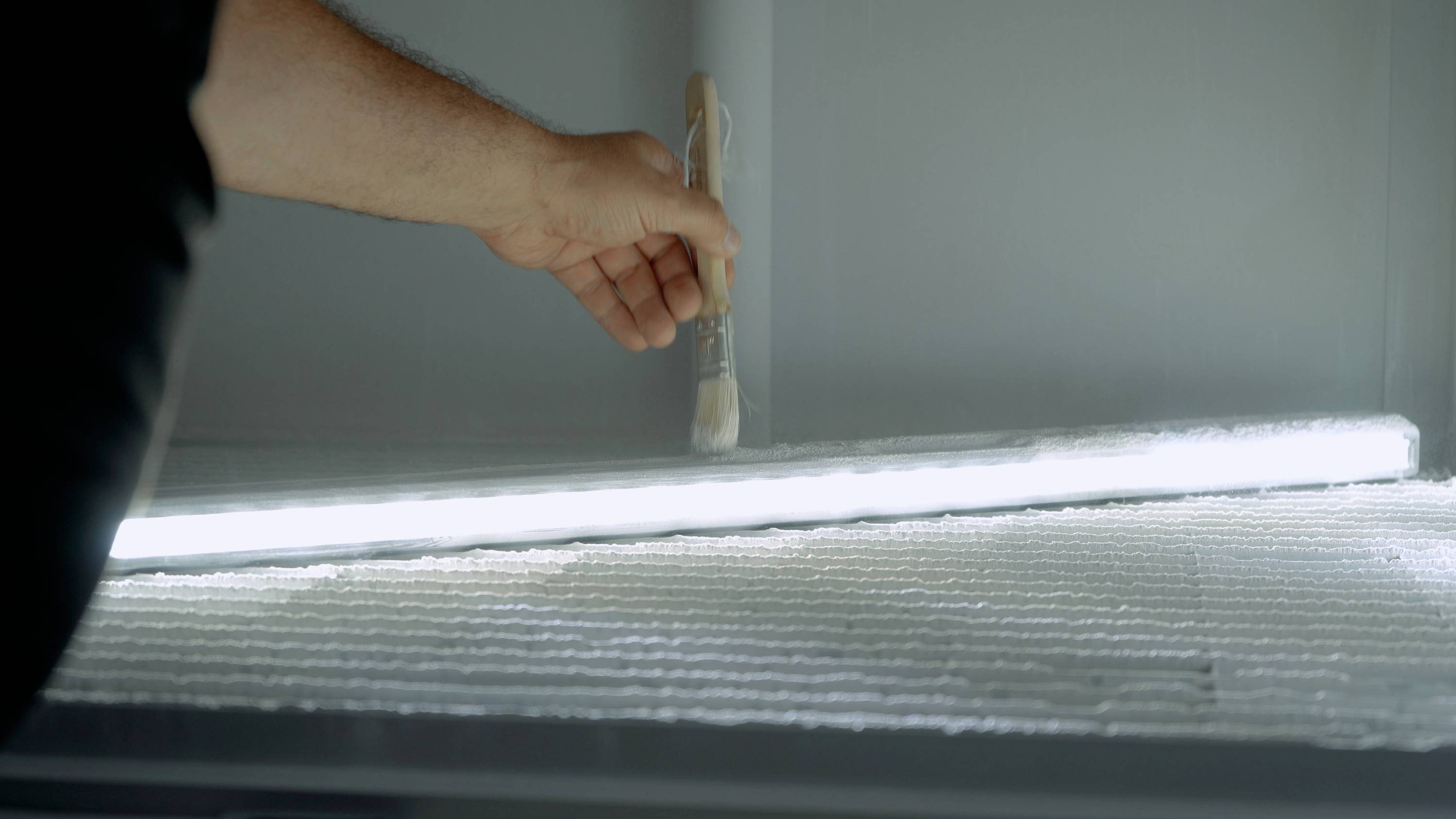 Une personne peint une lampe LED lumineuse fixée sur une surface texturée à l'aide d'un pinceau.