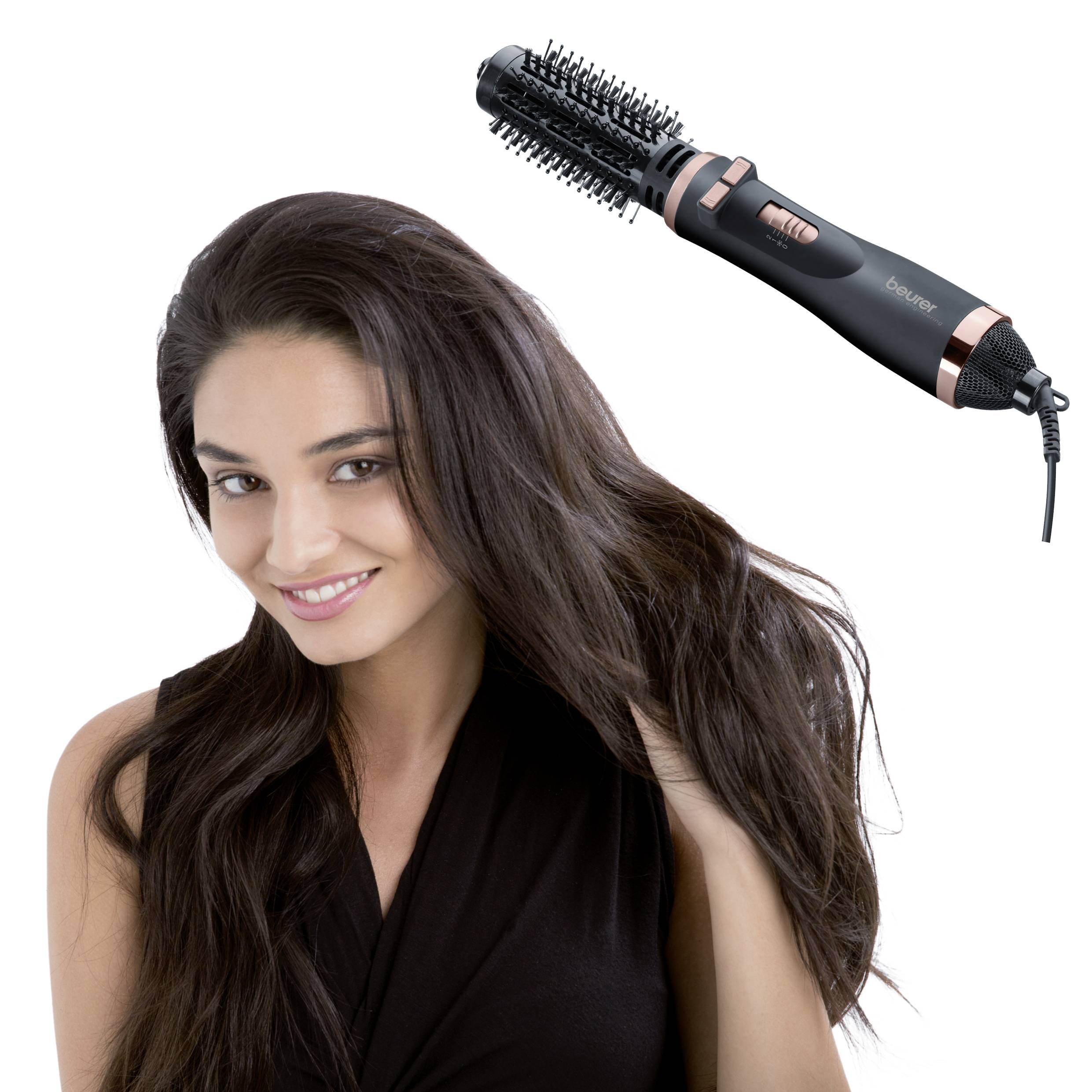 Une femme aux longs cheveux bruns utilise un sèche-cheveux à brosse rotative pour coiffer ses cheveux. L'appareil est noir et rose.