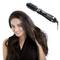 Une femme aux longs cheveux bruns utilise un sèche-cheveux à brosse rotative pour coiffer ses cheveux. L'appareil est noir et rose.