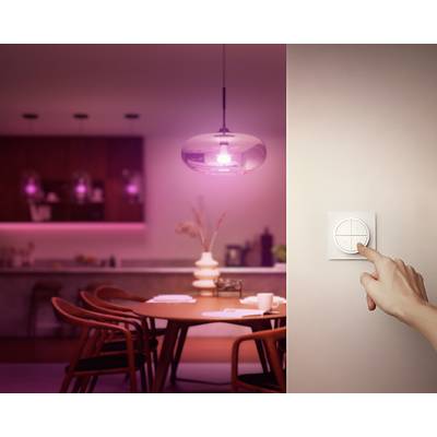 Une main actionne un interrupteur sur le mur, tandis qu'une salle à manger est éclairée en arrière-plan dans une lumière douce et chaleureuse.