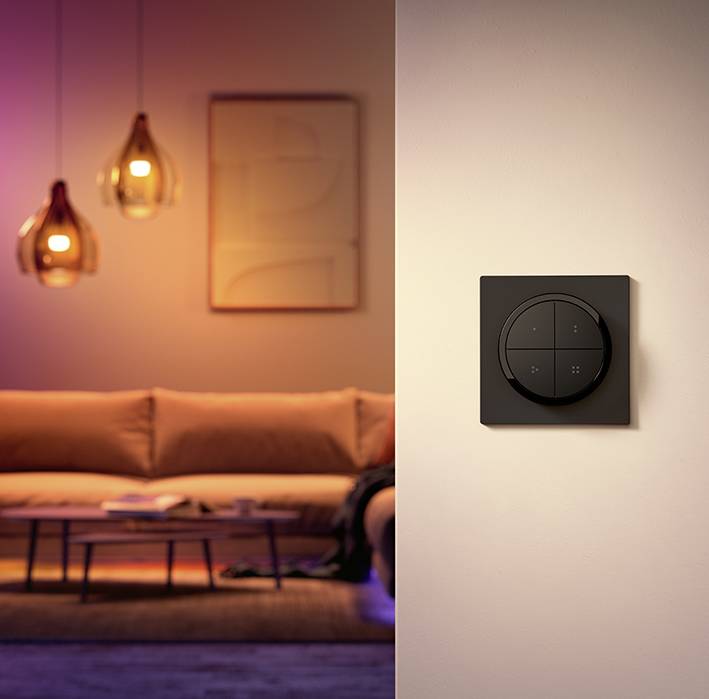 Un salon moderne avec un canapé et une table, au premier plan un interrupteur noir monté sur le mur avec plusieurs touches.
