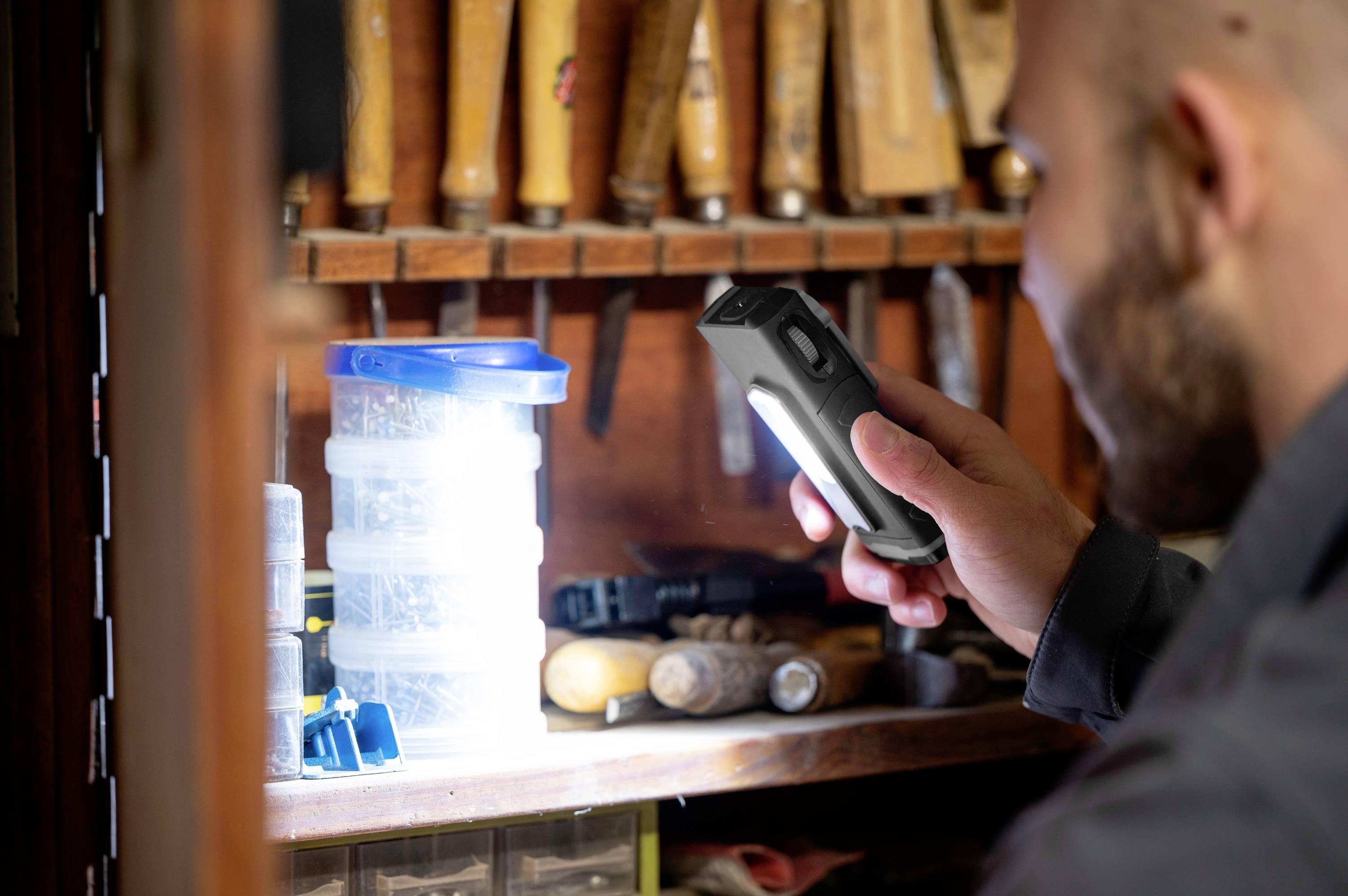 Une personne éclaire un armoire d'atelier avec une lampe de poche. Des outils et des contenants sont visibles en arrière-plan.