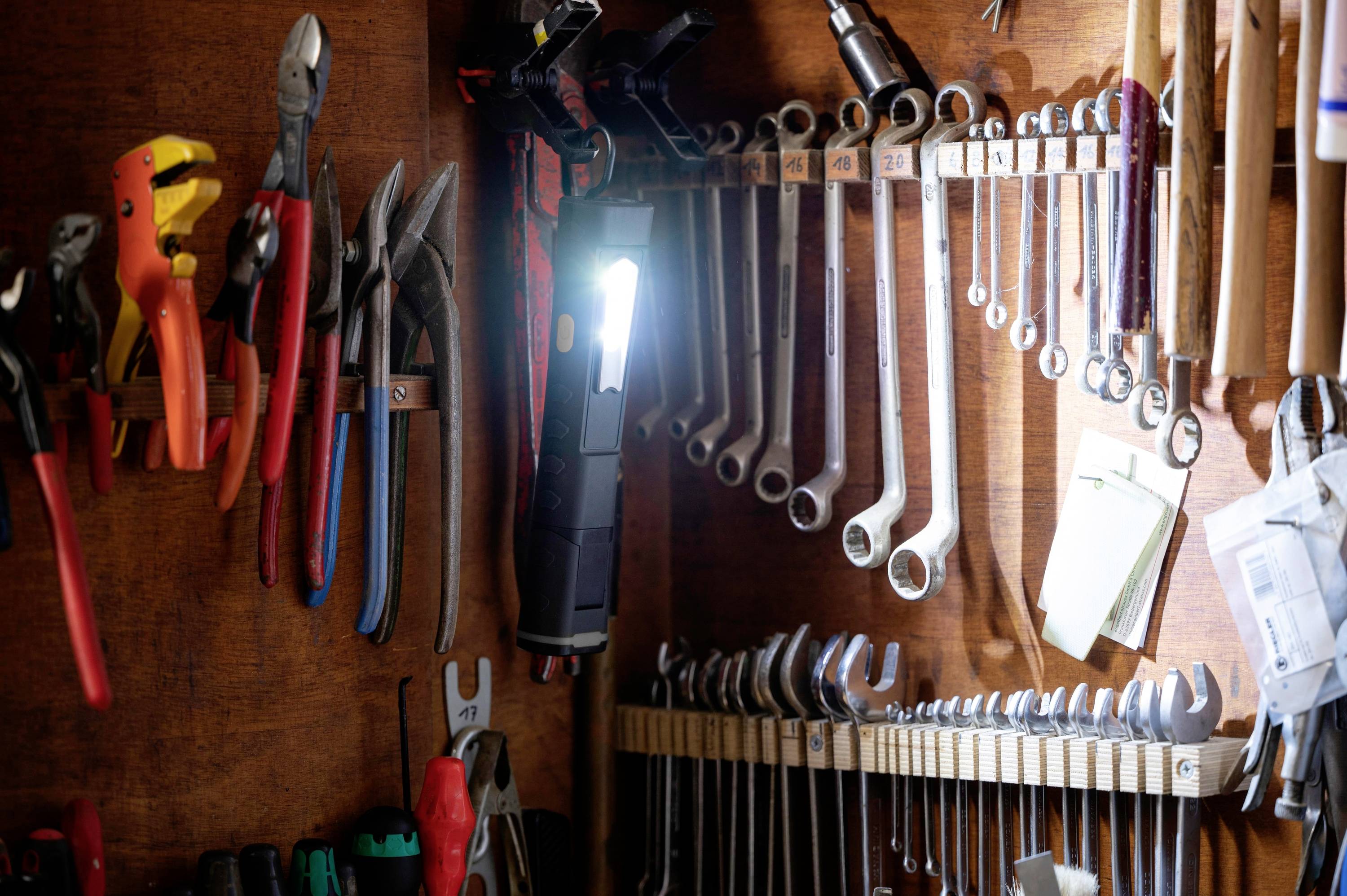 Différents outils sont soigneusement accrochés à un mur en bois lambris, notamment des pinces, des clés à molette et une lampe de poche.