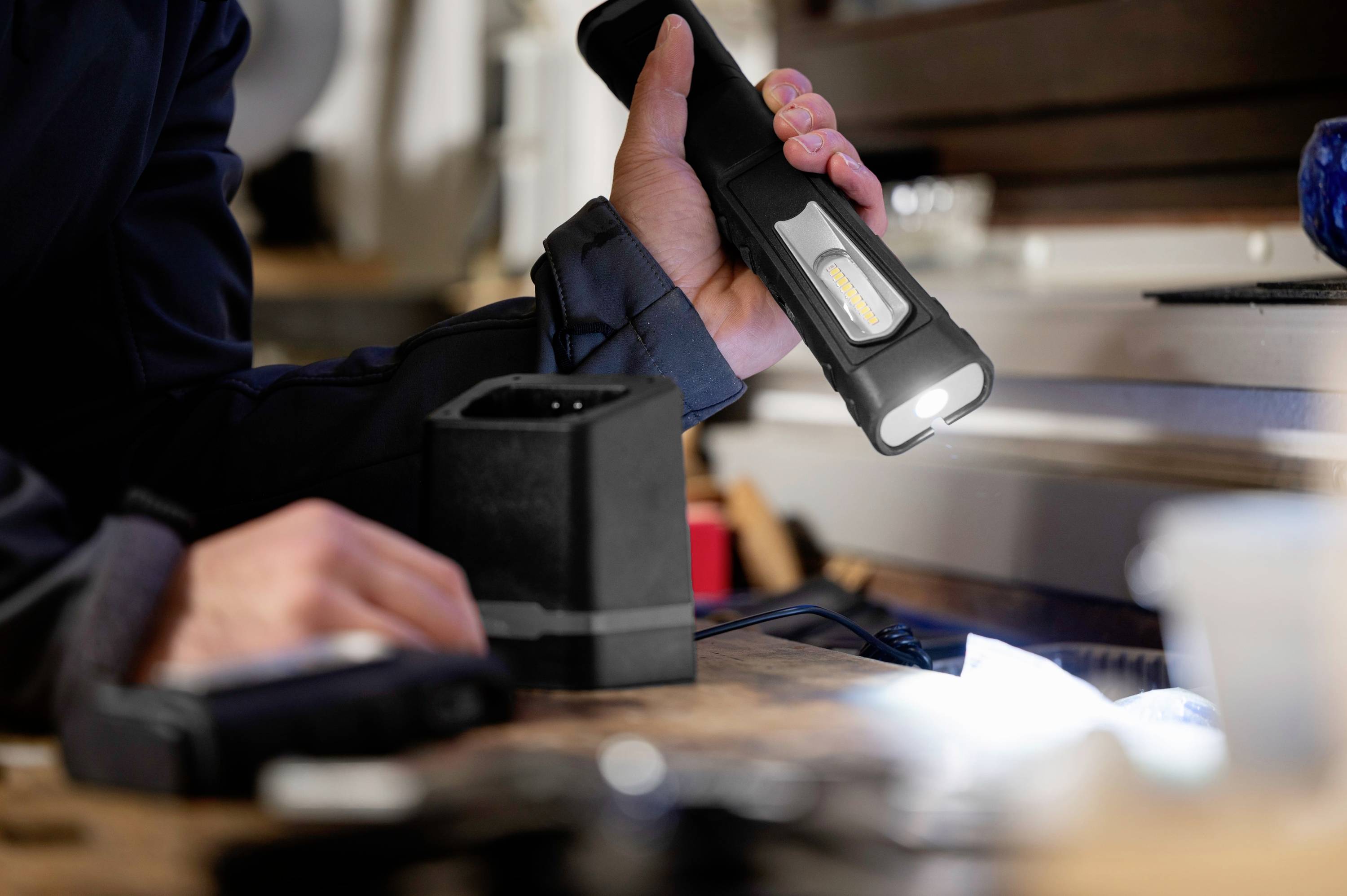 Une personne braque une lampe de poche sur une table de travail dans un atelier afin d'éclairer une zone spécifique.