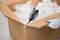 Une personne ouvre un carton à l'aide d'un cutter, à l'intérieur se trouvent des emballages en plastique.
