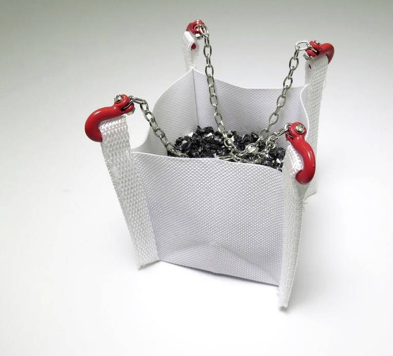 Un récipient blanc muni de boucles et de chaînes en métal rouge, rempli de matériaux noirs granuleux, sur un fond neutre.