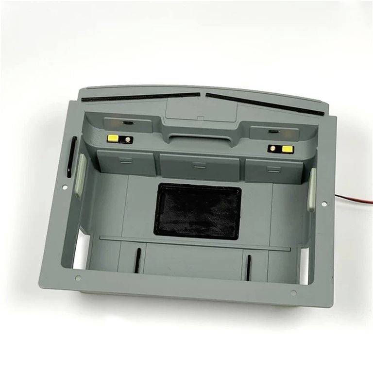 Boîtier en plastique gris, probablement une partie d'un appareil électronique, avec des trous et un rectangle noir au centre.