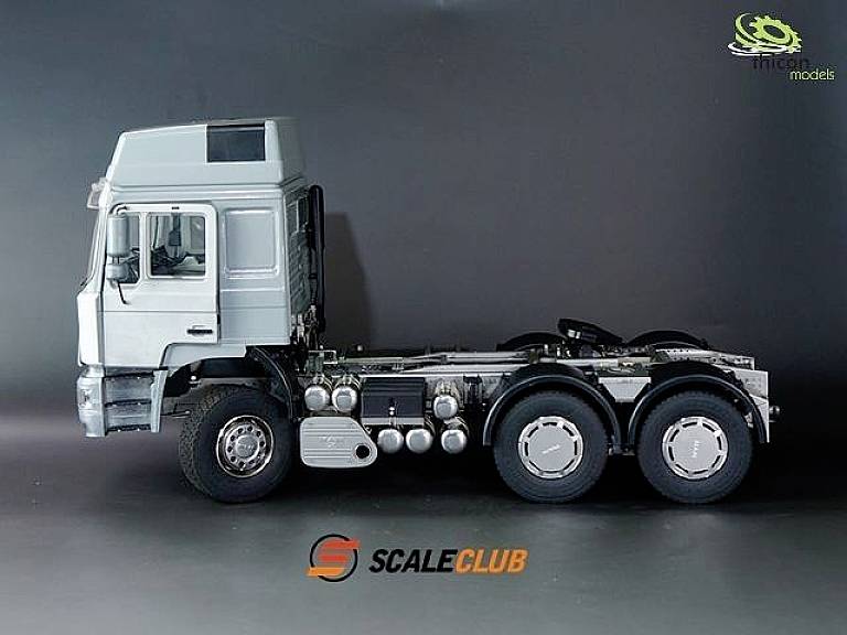 Modèle de camion à trois essieux, avec une cabine grise et un châssis détaillé sur un fond noir, logo de la marque en bas.