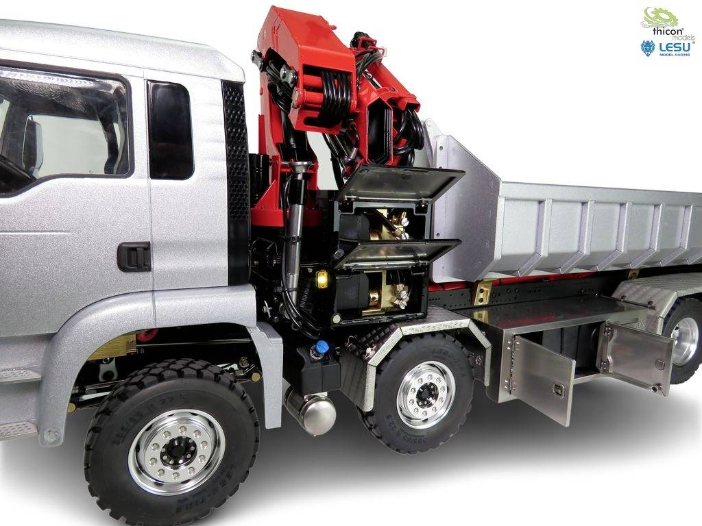 Camion avec une grue hydraulique et une plateforme de chargement. La grue est rouge, soulevée et prête à être utilisée. La cabine du conducteur est visible à gauche.