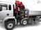 Camion avec une grue hydraulique et une plateforme de chargement. La grue est rouge, soulevée et prête à être utilisée. La cabine du conducteur est visible à gauche.