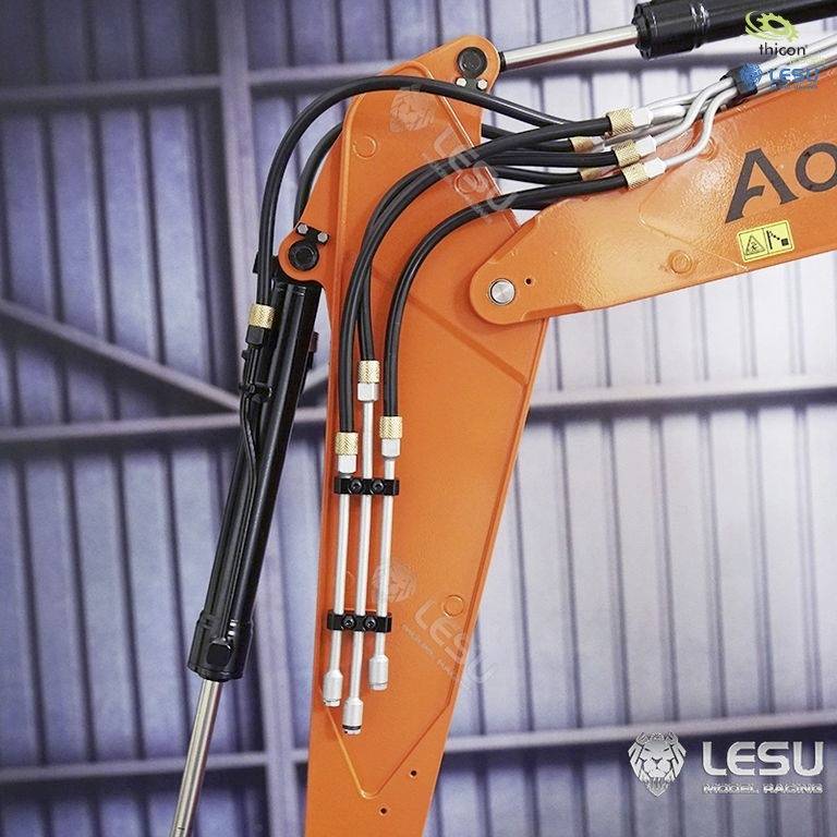 Un bras de pelle orange avec des conduites hydrauliques est visible de près. Il se détache sur un fond métallique.