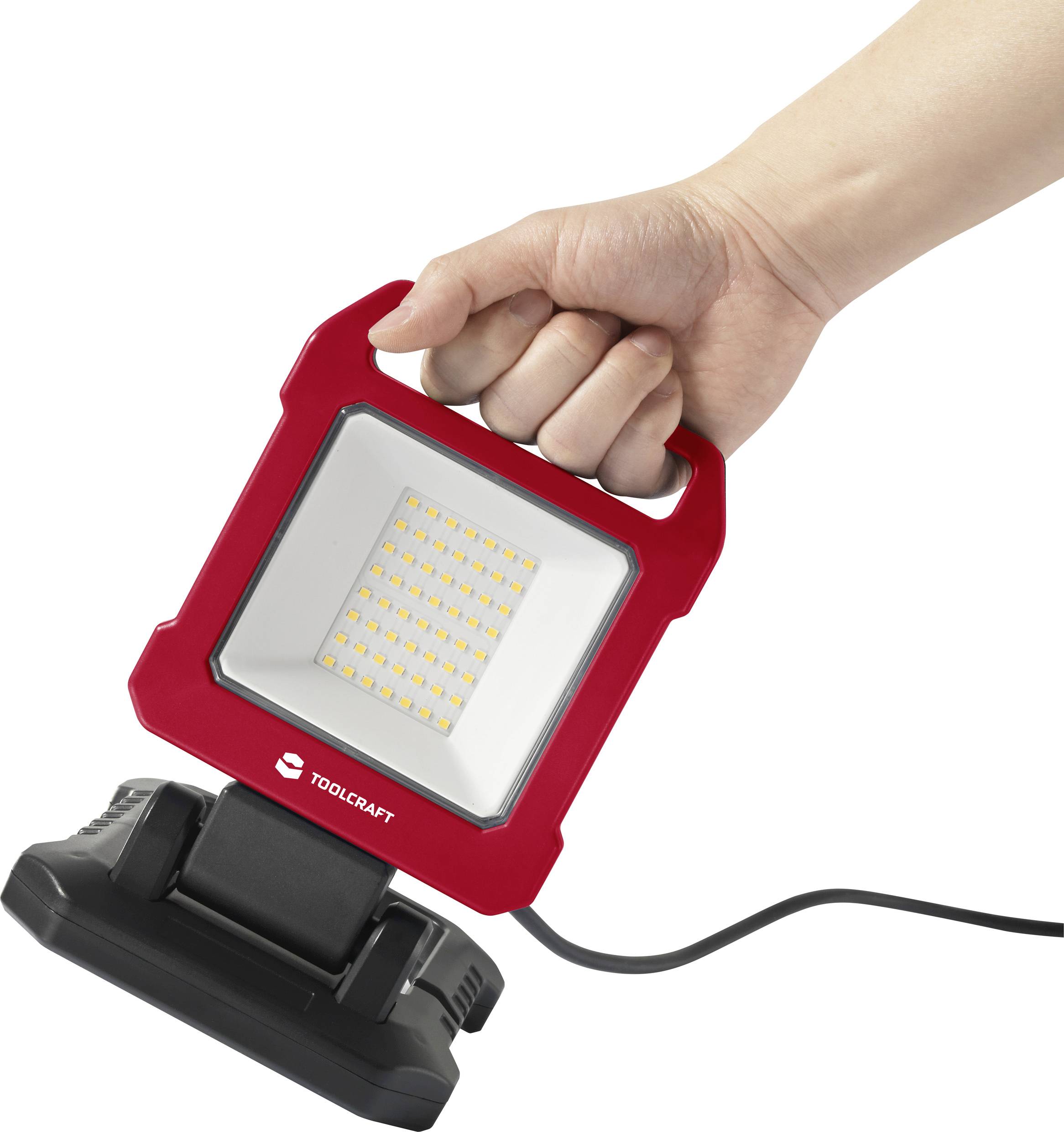 Une main tient un projecteur de travail LED portable rouge avec câble, adapté aux travaux manuels.
