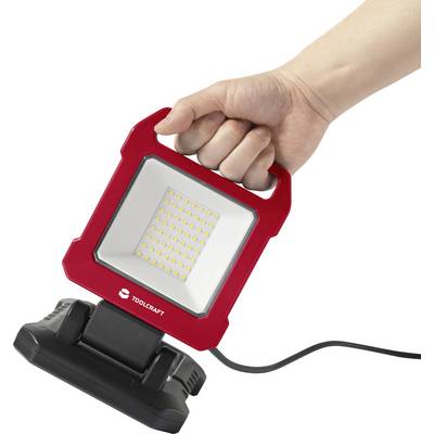 Une main tient un projecteur de travail LED portable rouge avec câble, adapté aux travaux manuels.