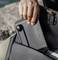Une main sort un appareil noir avec un petit levier d'un sac. Il semble s'agir d'un appareil électronique portable.
