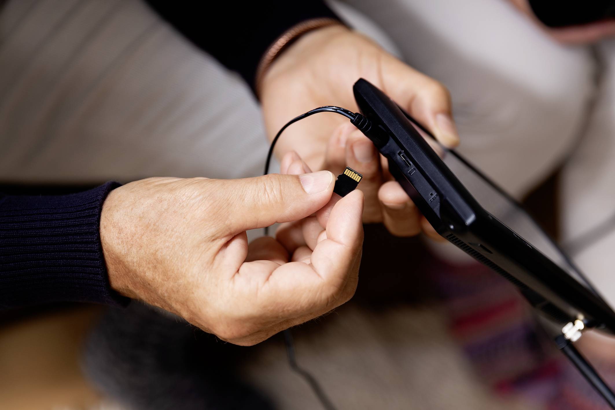 Une personne insère une carte mémoire dans un appareil portable, probablement une tablette.