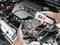 Une personne examine un moteur automobile à l'aide d'un smartphone et d'un endoscope. L'écran affiche une image en gros plan des pièces internes du moteur.