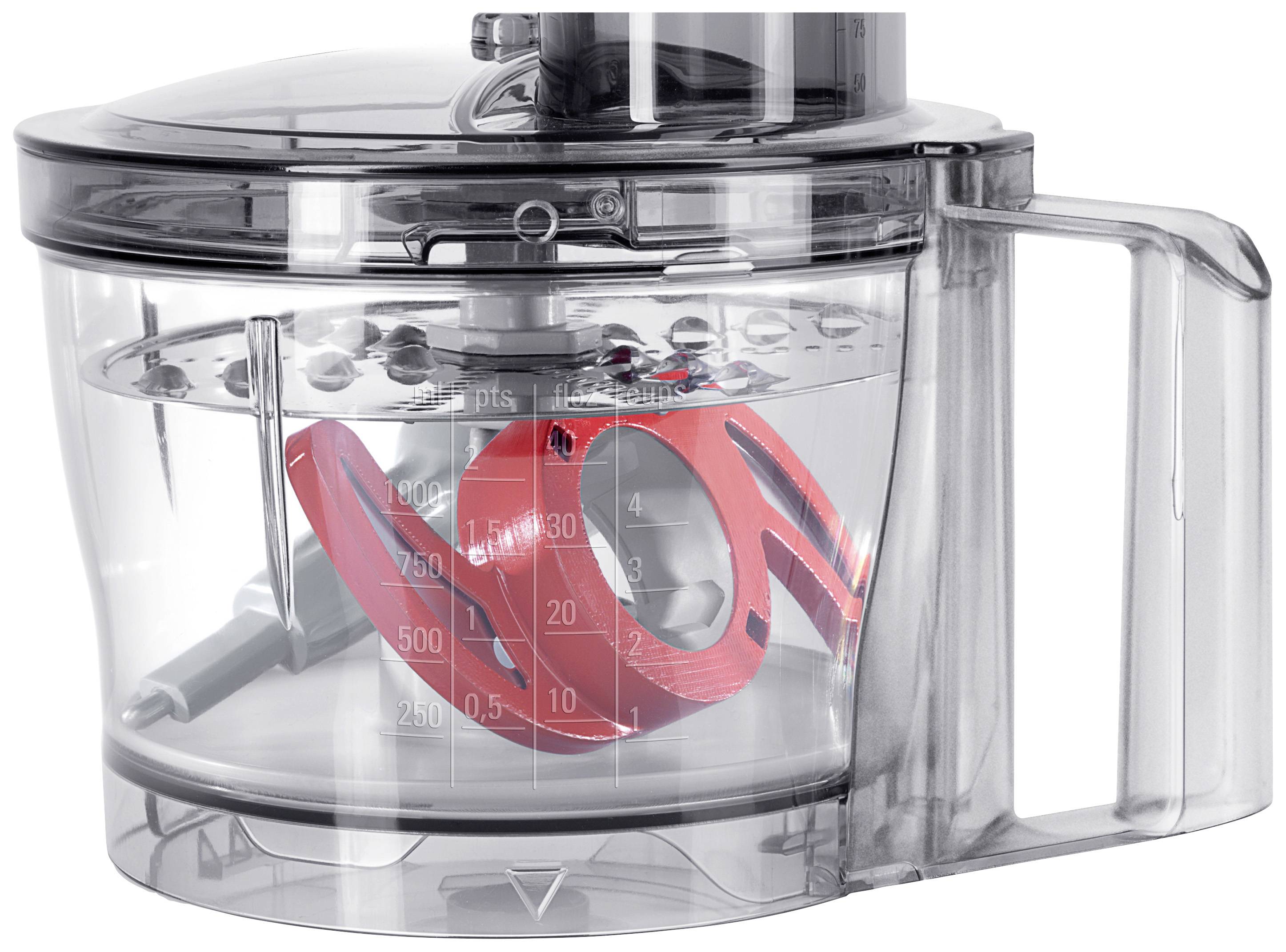 Machine de cuisine transparente avec des lames rotatives, offrant une vue intérieure de la fonction de coupe et de râpage, avec des graduations de mesure sur le côté.